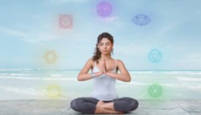 Image of a woman seated in a yoga posture with chakra symbols surrounding her, representing chakra balance during meditation.